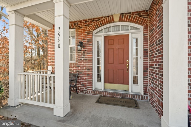 view of exterior entry featuring a porch and brick siding