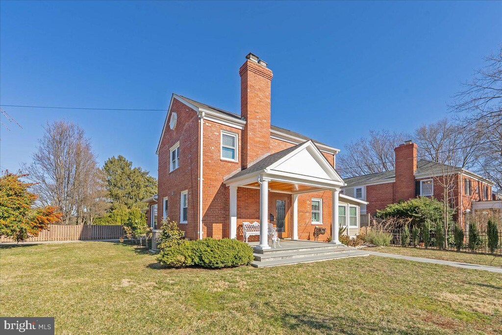 rear view of property with brick siding, a lawn, a chimney, and fence