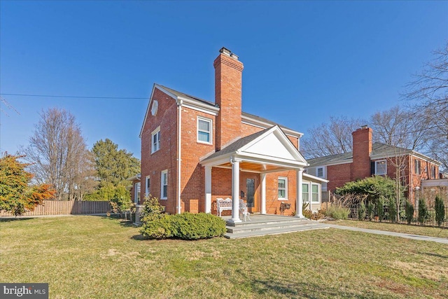 rear view of property with brick siding, a lawn, a chimney, and fence