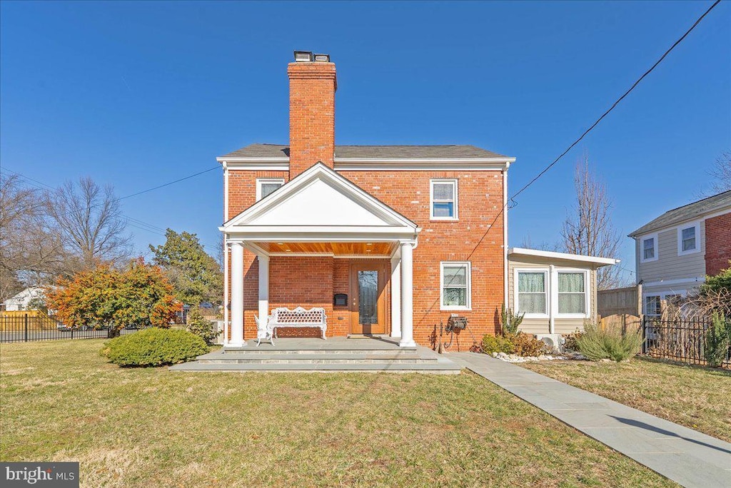 back of house with a porch, brick siding, fence, a yard, and a chimney