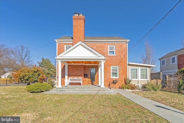 back of house with a porch, brick siding, fence, a yard, and a chimney