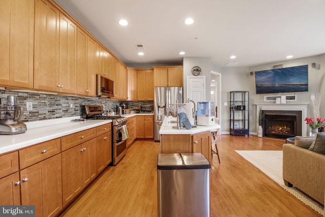 kitchen with light wood-style flooring, an island with sink, stainless steel appliances, decorative backsplash, and open floor plan