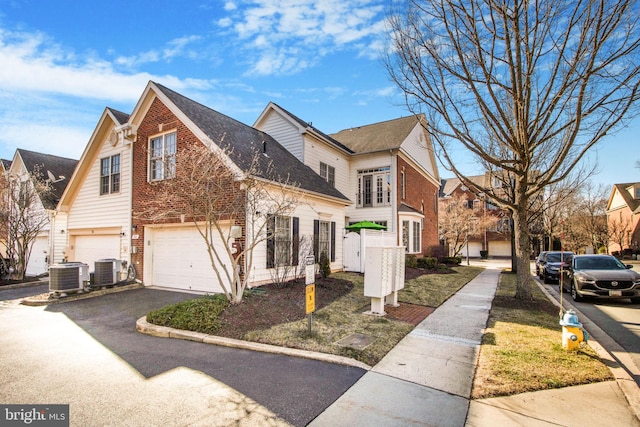 view of side of home with an attached garage, central AC unit, brick siding, and driveway