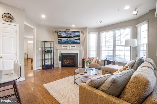 living room with recessed lighting, a warm lit fireplace, baseboards, and light wood-style floors