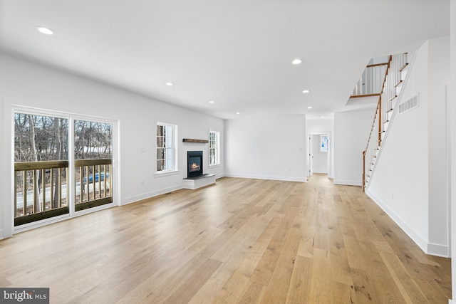 unfurnished living room featuring recessed lighting, visible vents, stairs, light wood-type flooring, and a glass covered fireplace