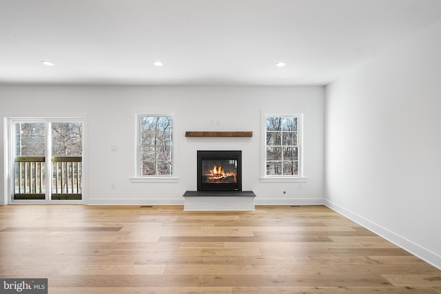 unfurnished living room with recessed lighting, a glass covered fireplace, a wealth of natural light, and light wood-style floors