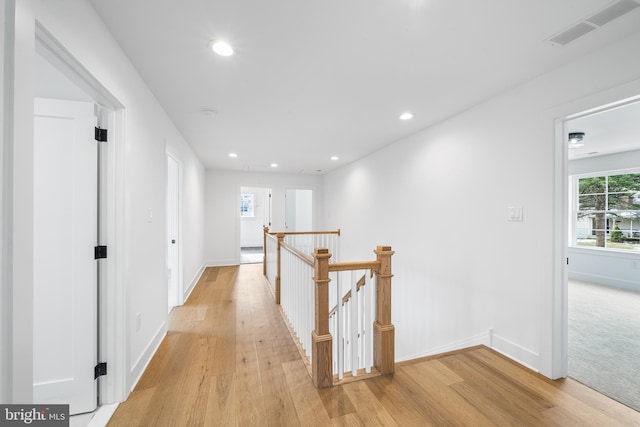 hall with light wood finished floors, recessed lighting, visible vents, and an upstairs landing