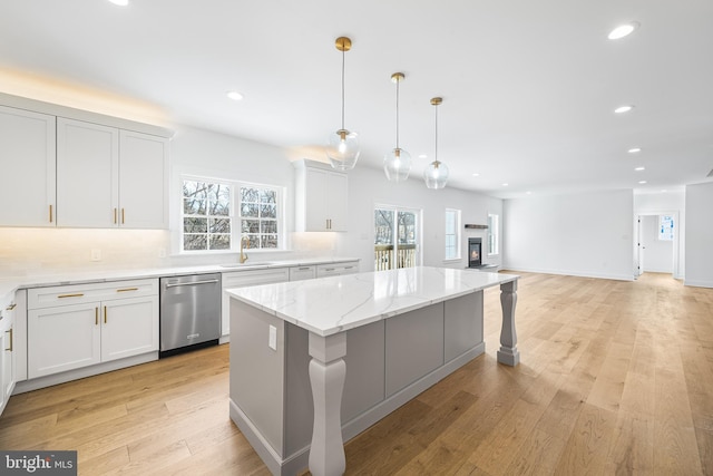 kitchen with light wood finished floors, light stone countertops, stainless steel dishwasher, a sink, and recessed lighting