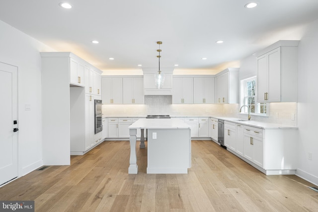 kitchen with light wood-style flooring, stainless steel appliances, light countertops, a center island, and tasteful backsplash