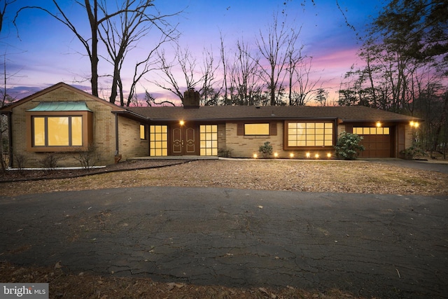 view of front of home with driveway, an attached garage, a chimney, and brick siding