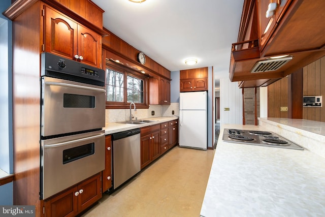 kitchen featuring tasteful backsplash, light countertops, appliances with stainless steel finishes, brown cabinetry, and a sink