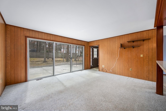 spare room featuring carpet floors, visible vents, and wood walls