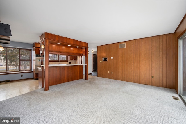 unfurnished living room with carpet, wooden walls, and visible vents