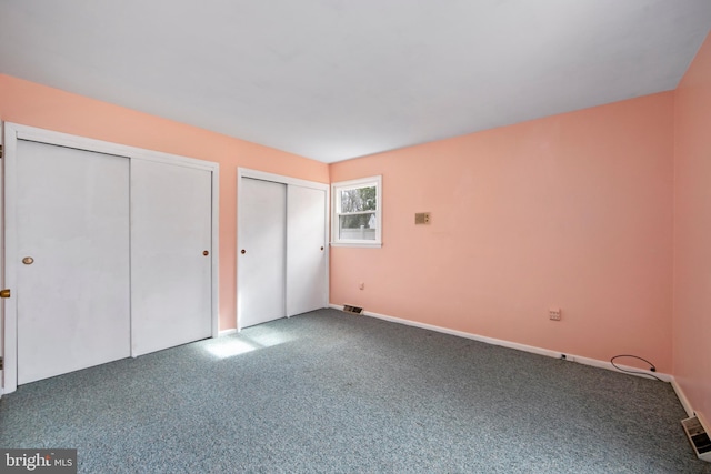 unfurnished bedroom featuring baseboards, carpet floors, visible vents, and multiple closets