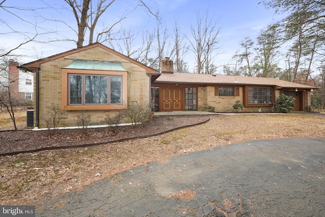 view of front of house with a garage, a chimney, central AC, and brick siding