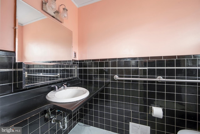 bathroom featuring ornamental molding, wainscoting, visible vents, and a sink