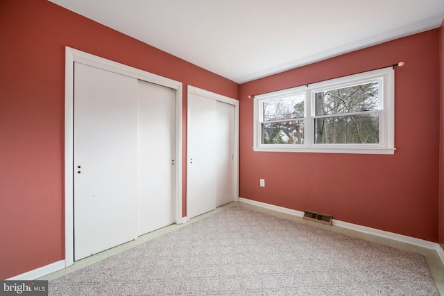 unfurnished bedroom featuring carpet floors, baseboards, visible vents, and two closets