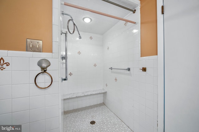 full bath featuring a tile shower, tile walls, and wainscoting