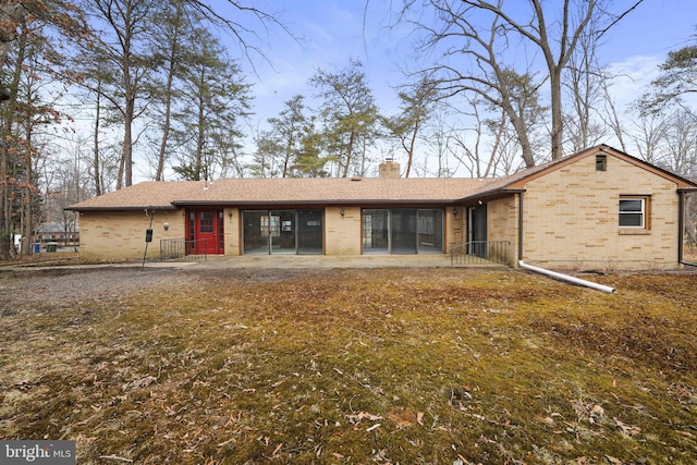 view of front of house featuring a patio area, brick siding, and a chimney