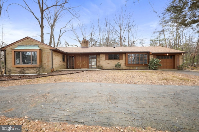 ranch-style home featuring aphalt driveway, brick siding, a chimney, and an attached garage