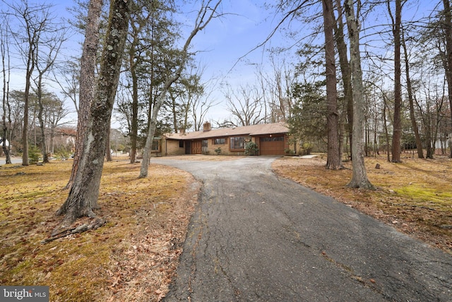 view of front facade featuring aphalt driveway, a chimney, and an attached garage