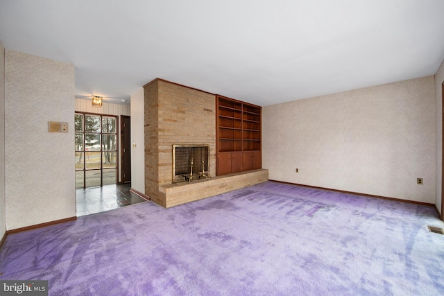 unfurnished living room with carpet floors, built in shelves, a fireplace, visible vents, and baseboards