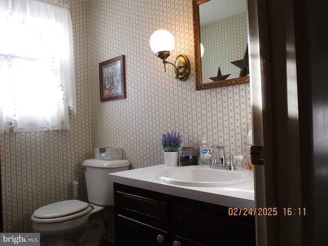 half bathroom with toilet, vanity, and wallpapered walls