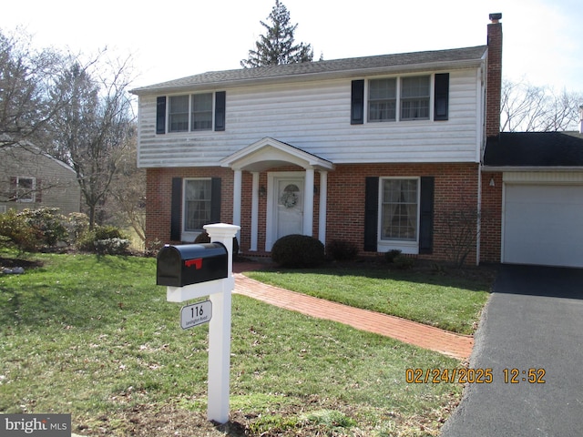 colonial home featuring a front yard, brick siding, a chimney, and an attached garage