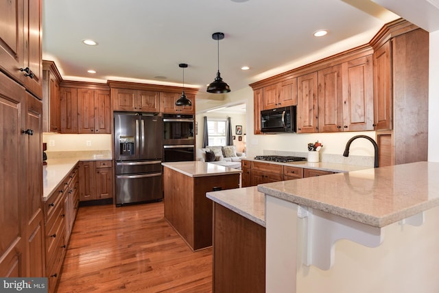 kitchen featuring light stone counters, a center island, a peninsula, decorative light fixtures, and black appliances