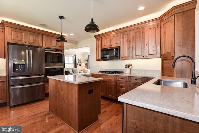 kitchen with stainless steel appliances, a sink, hanging light fixtures, and light stone counters