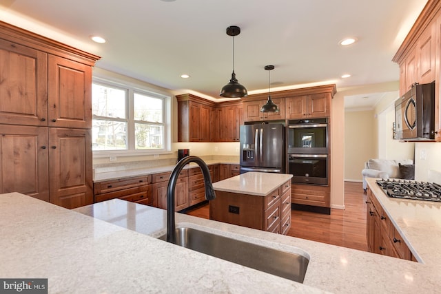 kitchen with appliances with stainless steel finishes, a kitchen island, a sink, and light stone counters