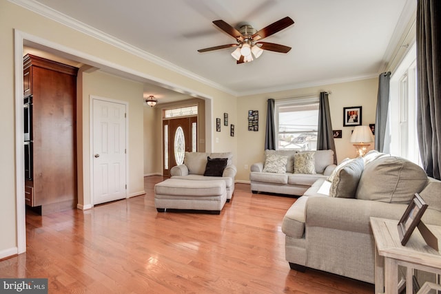 living area featuring ceiling fan, ornamental molding, light wood-style flooring, and baseboards