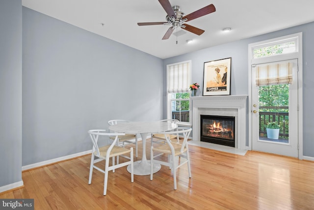 dining space featuring a ceiling fan, a fireplace with flush hearth, hardwood / wood-style flooring, and baseboards