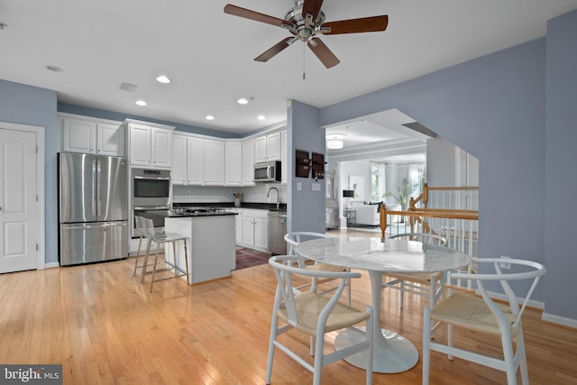 kitchen with light wood finished floors, dark countertops, appliances with stainless steel finishes, white cabinets, and a kitchen island