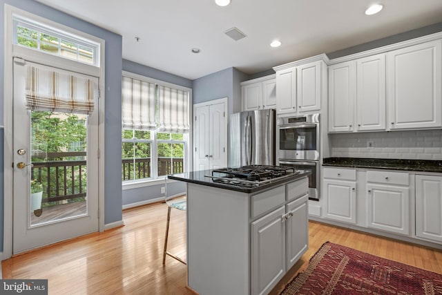 kitchen with tasteful backsplash, white cabinets, light wood-style flooring, a center island, and stainless steel appliances