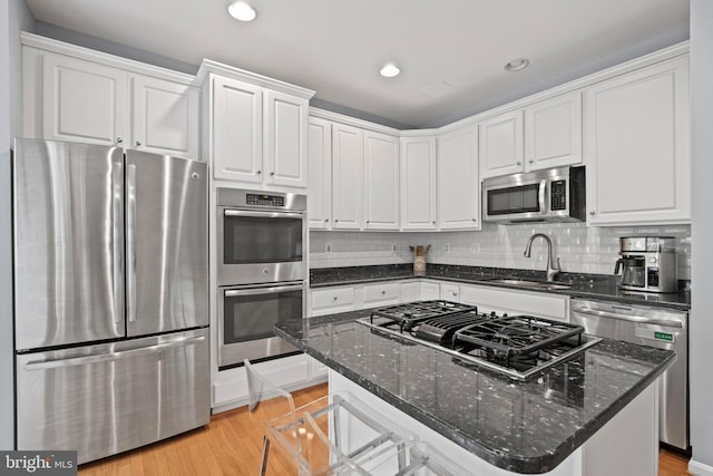 kitchen featuring light wood finished floors, white cabinets, a sink, stainless steel appliances, and backsplash