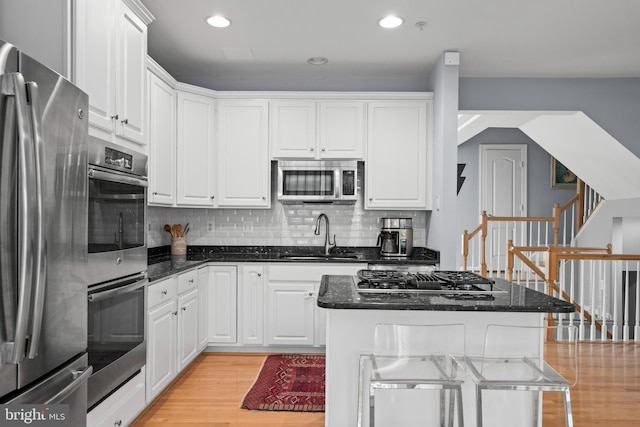 kitchen with a sink, white cabinetry, appliances with stainless steel finishes, light wood-type flooring, and tasteful backsplash