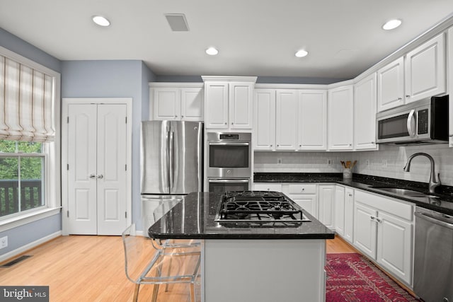 kitchen featuring stainless steel appliances, a sink, visible vents, white cabinetry, and backsplash