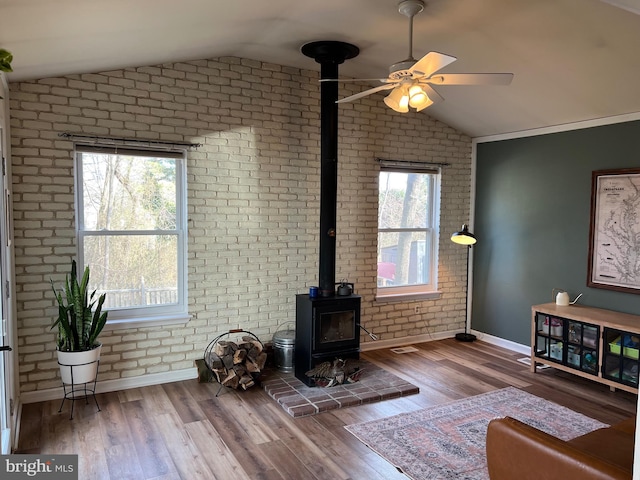 living room with a ceiling fan, lofted ceiling, brick wall, wood finished floors, and a wood stove