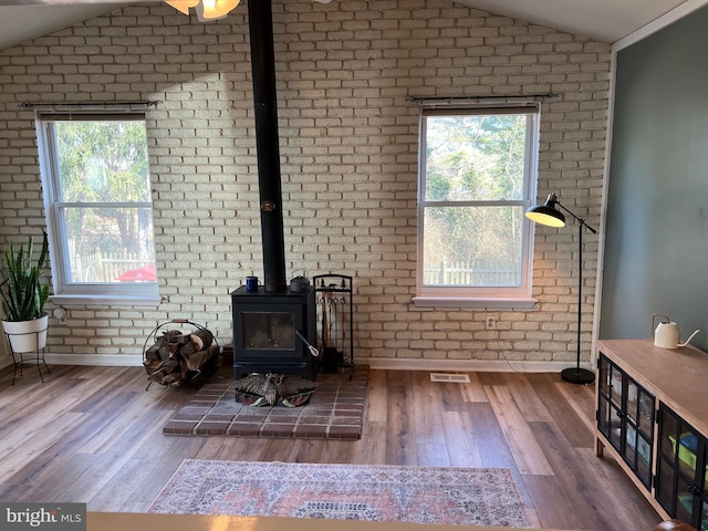 living room with a wood stove, vaulted ceiling, a wealth of natural light, and wood finished floors