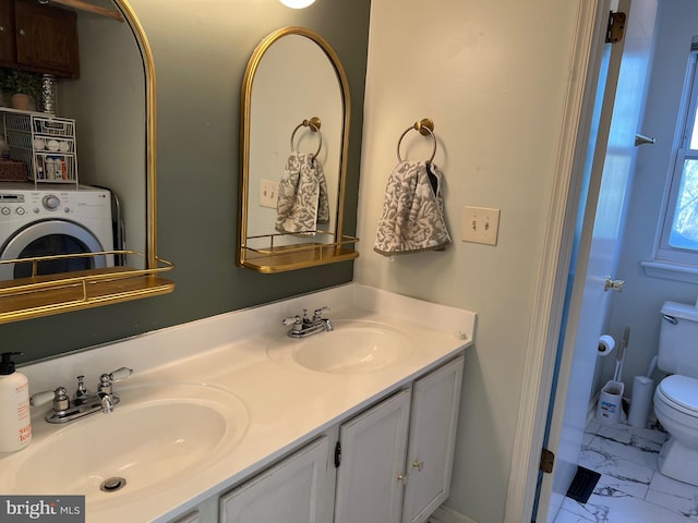 bathroom with toilet, washer / dryer, marble finish floor, and a sink