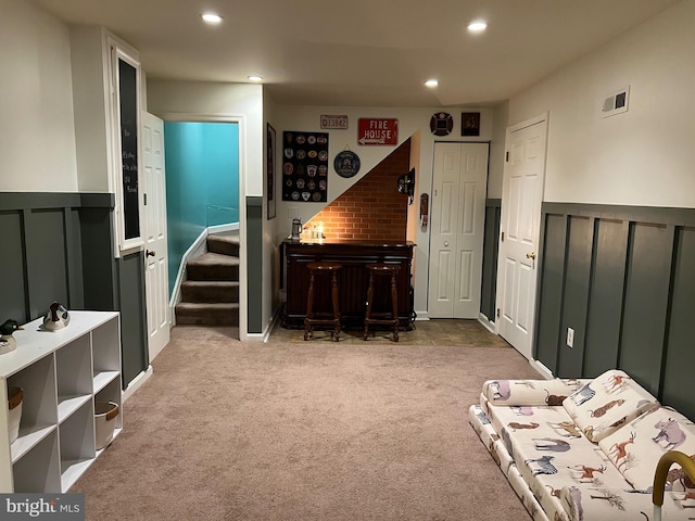 living area with carpet flooring, visible vents, stairway, wainscoting, and a bar