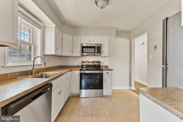 kitchen with tasteful backsplash, white cabinets, stainless steel appliances, light countertops, and a sink