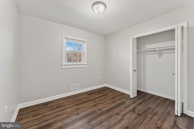 unfurnished bedroom featuring a closet, dark wood finished floors, visible vents, and baseboards