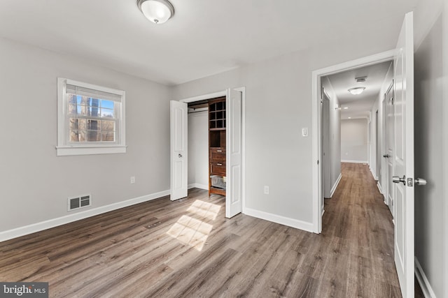 unfurnished bedroom with a closet, visible vents, baseboards, and wood finished floors