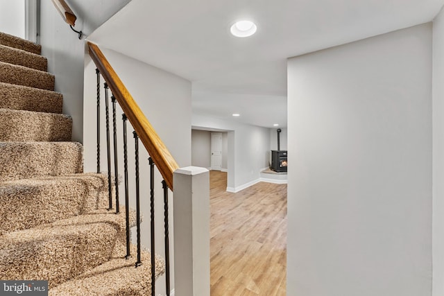 stairway with baseboards, wood finished floors, a wood stove, and recessed lighting