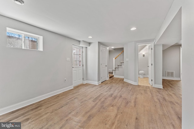 below grade area with light wood-style floors, visible vents, stairway, and baseboards