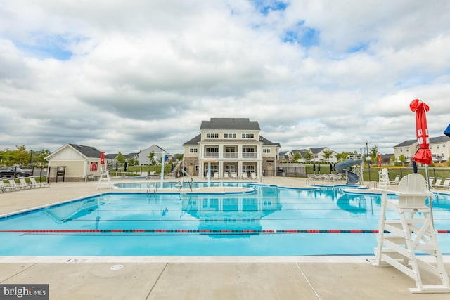 community pool with fence, a water slide, and a patio