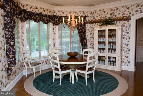 dining area with ornamental molding, wood finished floors, a chandelier, and wallpapered walls