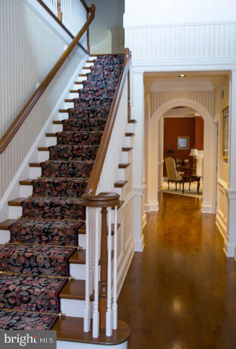 staircase with arched walkways, wood finished floors, a towering ceiling, and a decorative wall